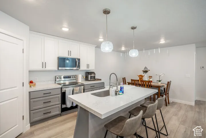 Kitchen featuring two-tone cabinetry, quartz countertops, central island with stainless steel sink, stainless steel appliances, and wood-finish flooring