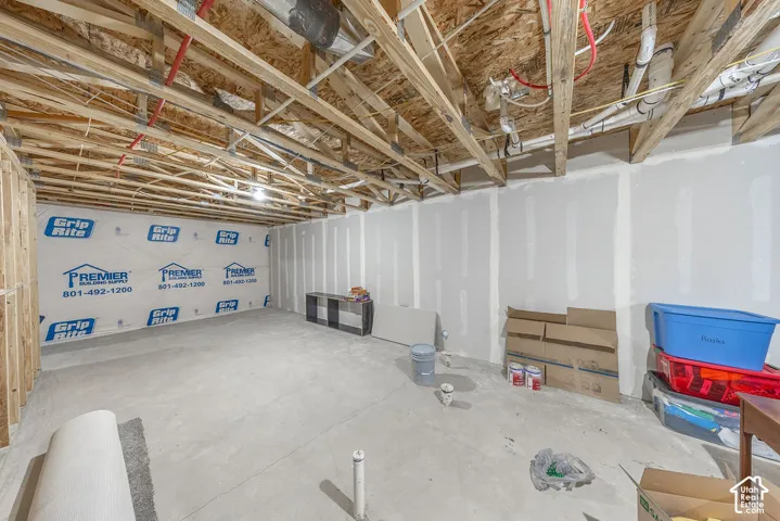 Unfinished area featuring exposed wooden ceiling joists, concrete flooring, and partial drywall installation