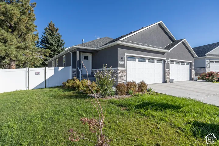 Single-story exterior featuring dark gray stucco siding, stone veneer accents, a multi-car garage, and white vinyl privacy fencing