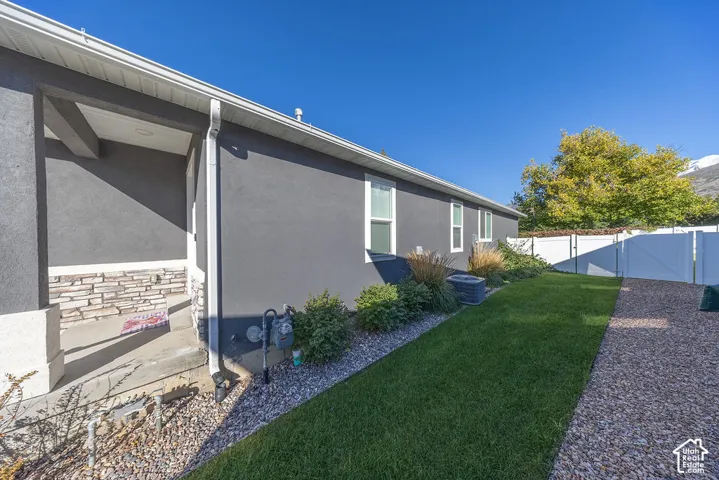 Exterior profile featuring dark gray stucco siding, stone veneer accents, concrete covered porch, manicured lawn, and white vinyl privacy fencing