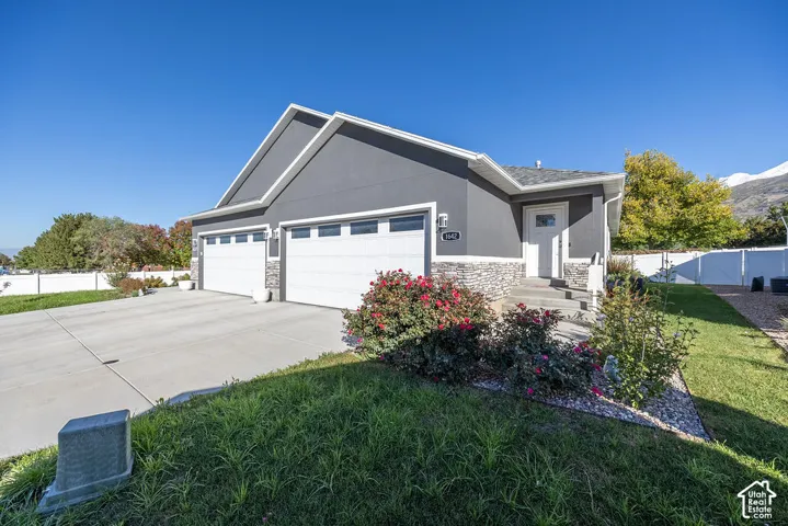 Exterior featuring stucco siding, stone veneer accents, two-car garage, concrete driveway, and white privacy fencing