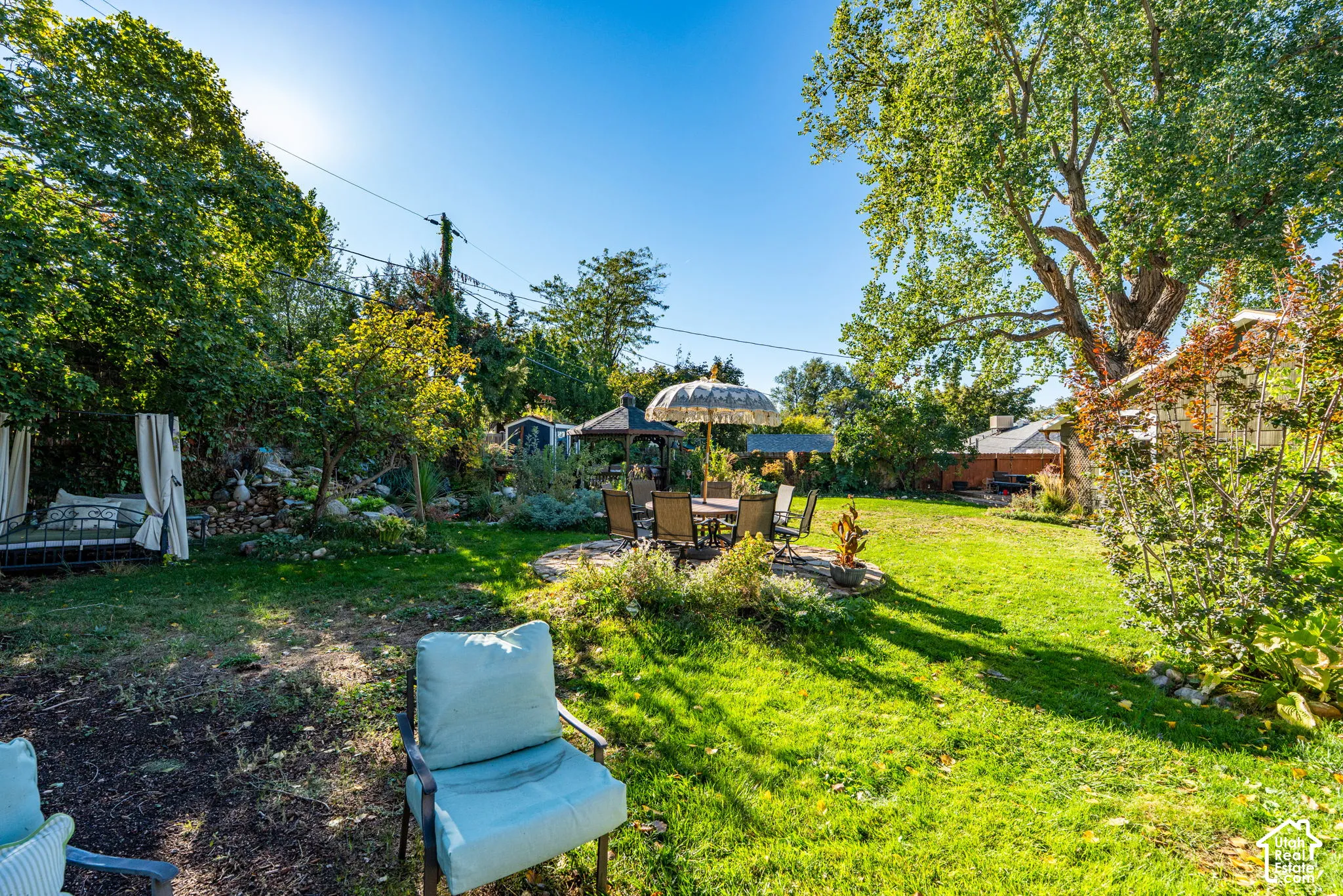 Expansive backyard featuring a natural stone patio, a wooden gazebo, mature canopy trees, and established landscaping