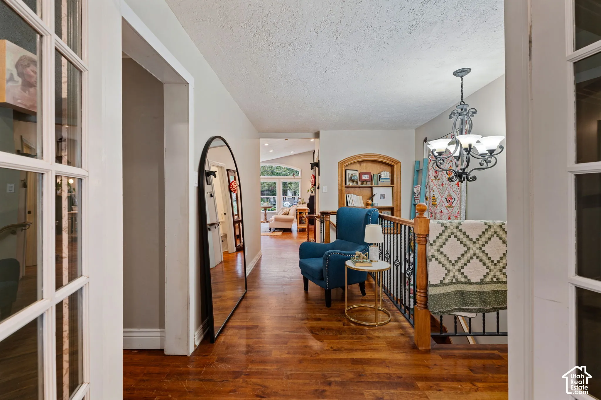 Wood-finish flooring, built-in recessed shelving, iron and wood staircase railing, and decorative multi-arm chandelier