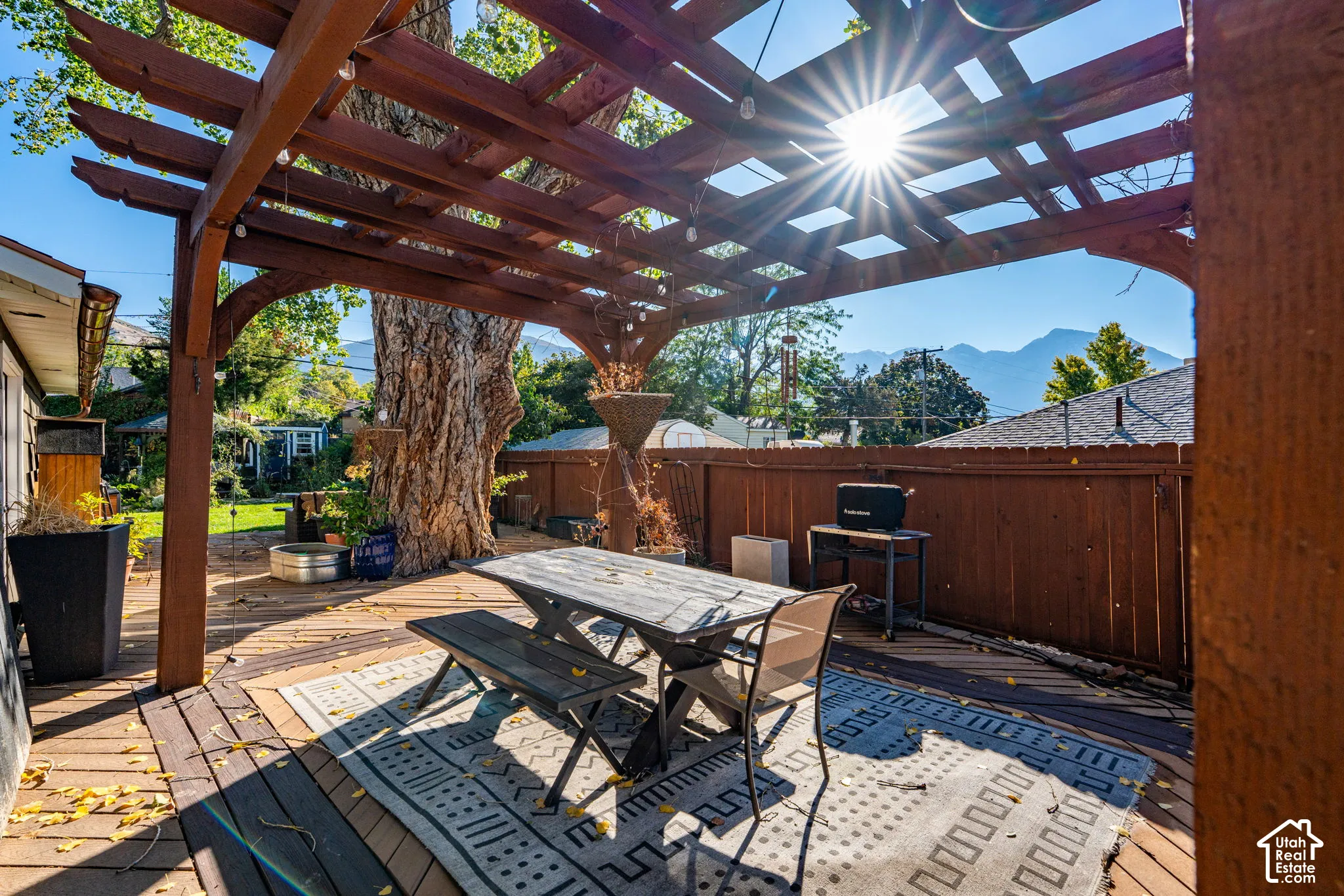 Outdoor wooden pergola covering a spacious deck, defined by a wood-plank surface and mountain backdrop