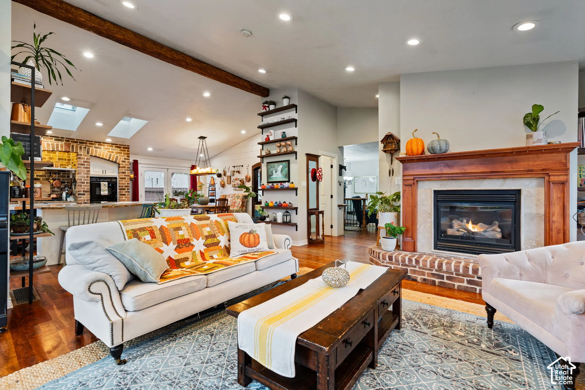 Exposed wood ceiling beams, recessed lighting, brick-surround gas fireplace with a wood mantel, built-in shelving, and skylights