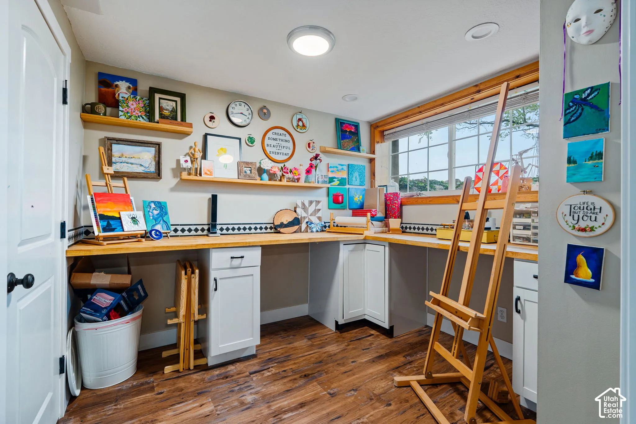 Built-in workspace featuring wood-finish countertops, white cabinetry with matte black hardware, floating wood shelving, and wood-finish flooring