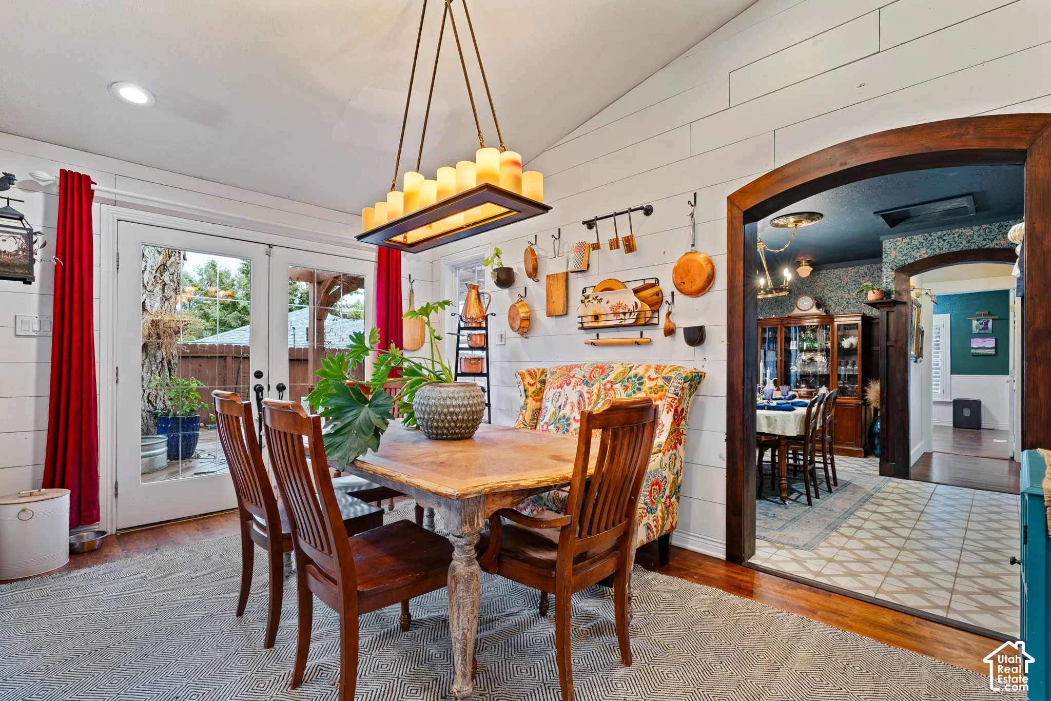 Vaulted ceiling with horizontal plank wall paneling, rectangular multi-light pendant fixture, wood-finish flooring, and a decorative arched wood entryway