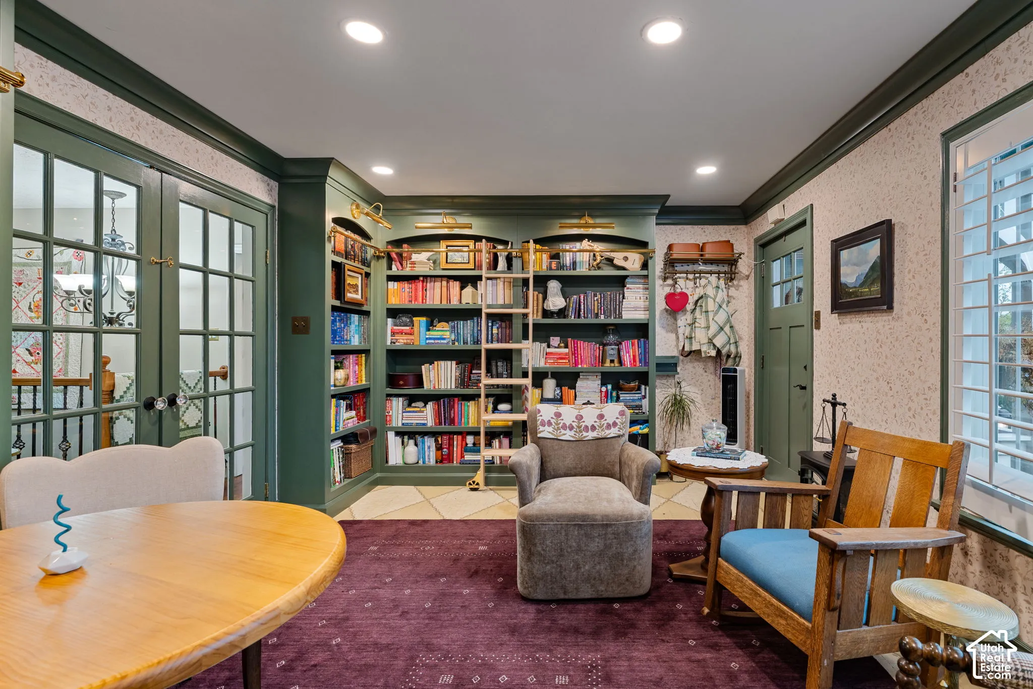 Custom floor-to-ceiling built-in shelving with integrated brass ladder and rail, recessed lighting, multi-pane glass French doors, and plantation shutters