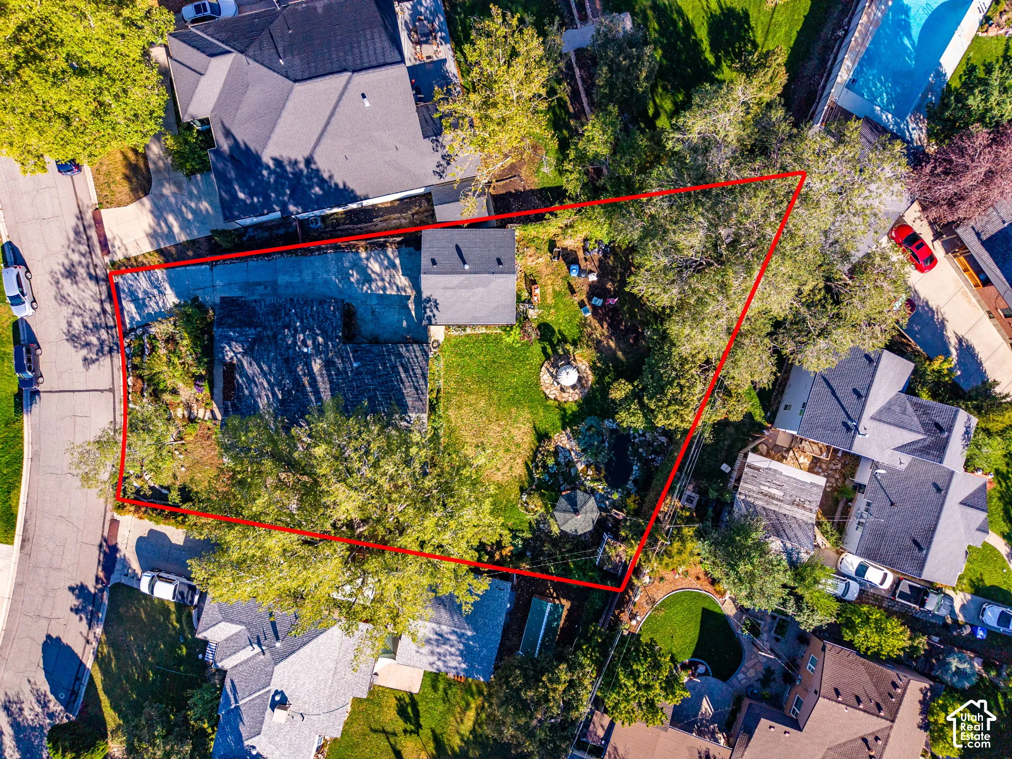 Aerial perspective of a property lot featuring an expansive lawn, mature tree canopy, stone-bordered landscaping, and a concrete driveway