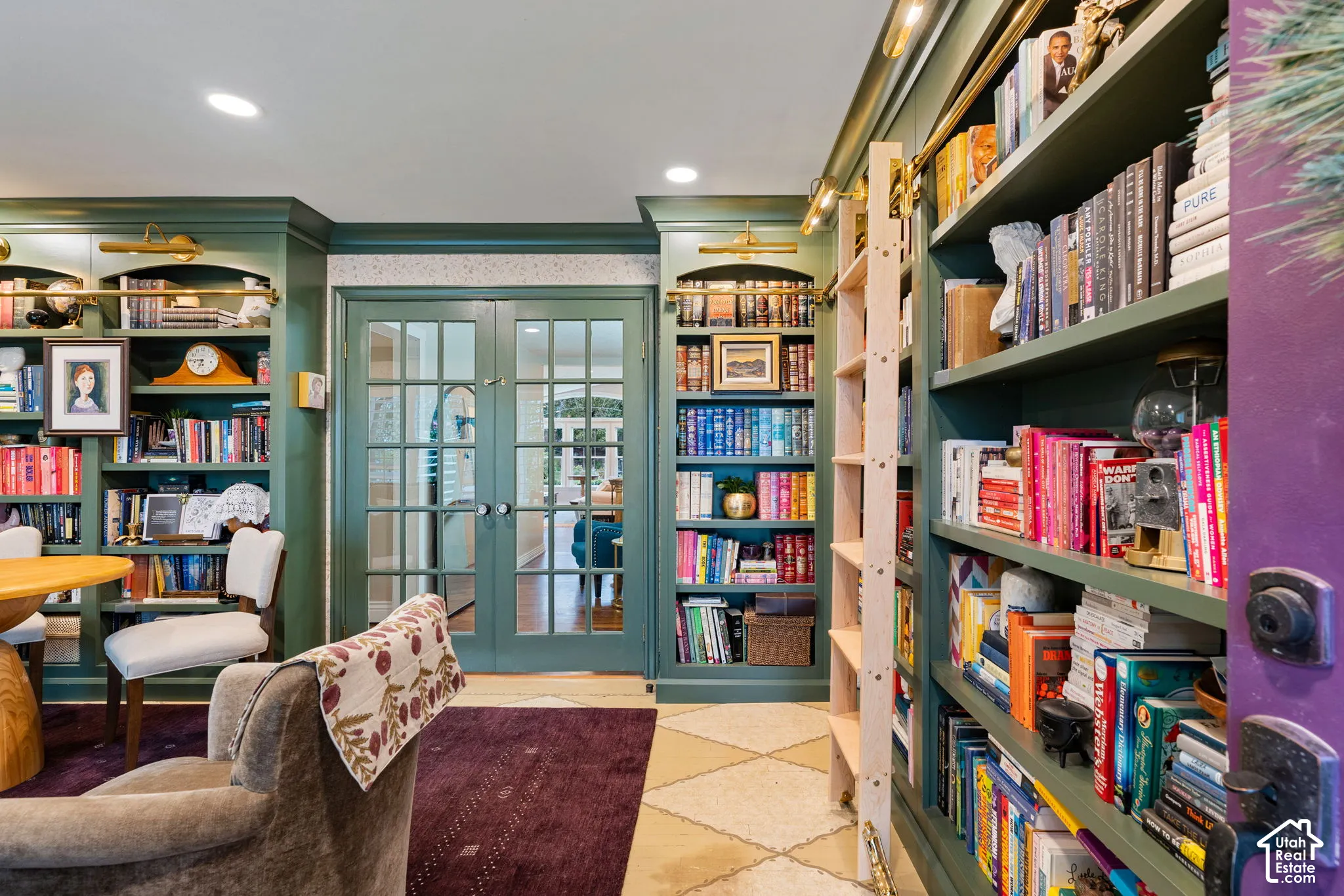 Floor-to-ceiling built-in cabinetry with integrated library lighting, rolling library ladder, and French doors