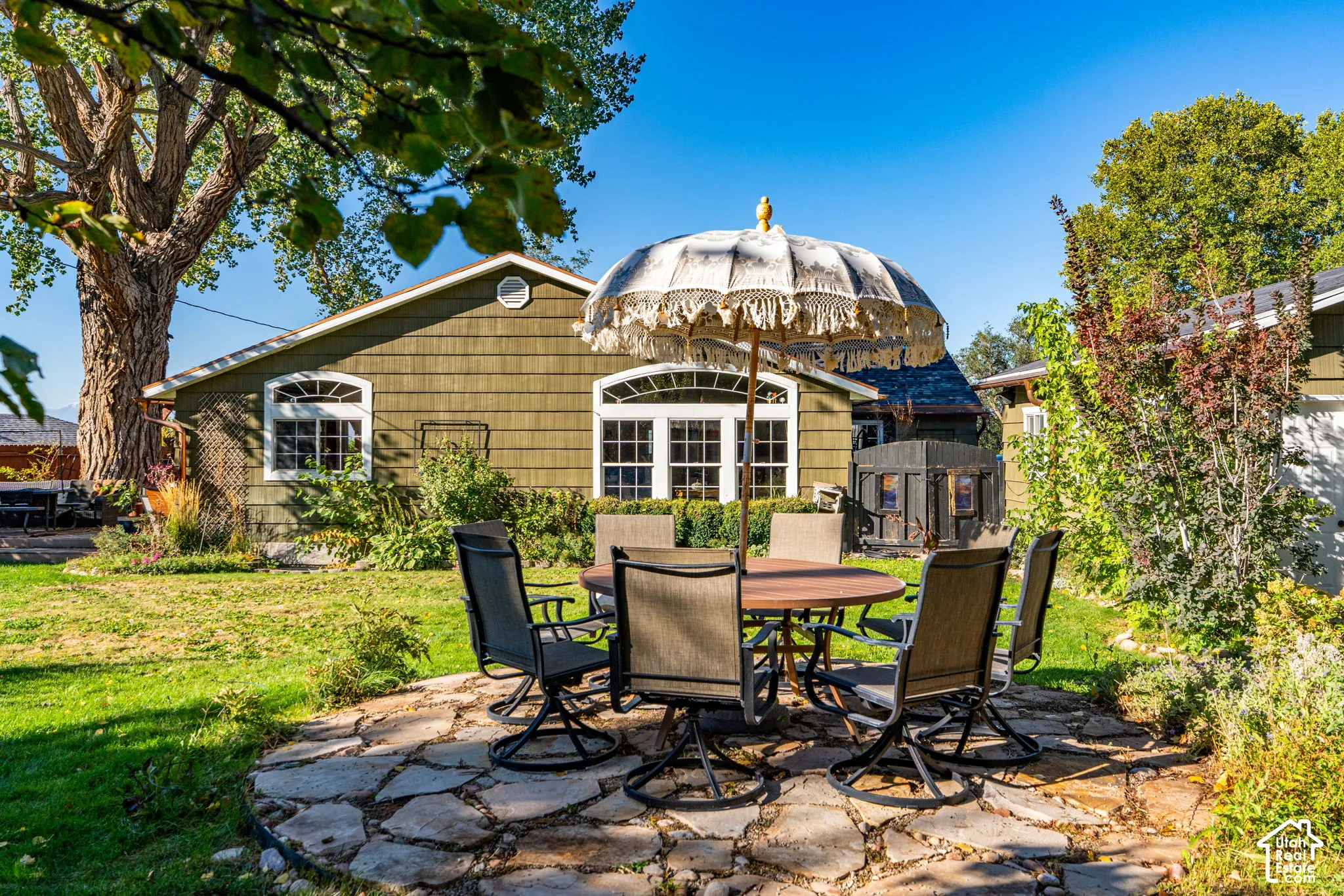 Backyard featuring a stone patio, shake-style siding, arched multi-pane windows, and mature trees
