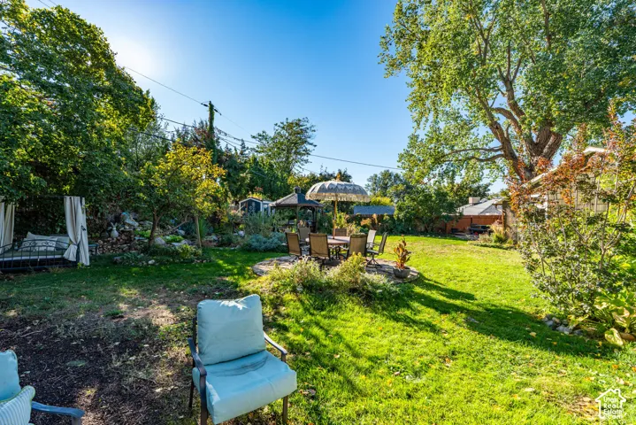 Expansive backyard featuring a natural stone patio, a wooden gazebo, mature canopy trees, and established landscaping