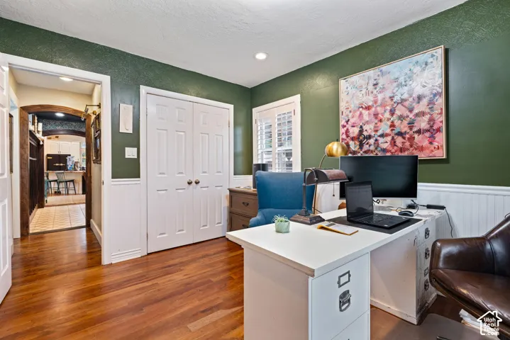 Room with wood-finish flooring, white beadboard wainscoting, recessed ceiling lighting, and plantation shutters