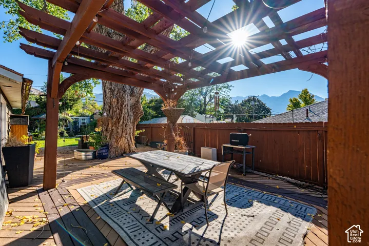 Outdoor wooden pergola covering a spacious deck, defined by a wood-plank surface and mountain backdrop