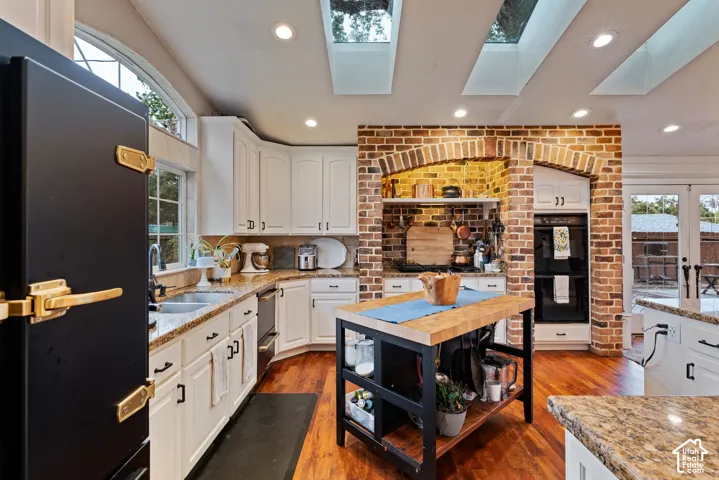 Kitchen featuring white cabinetry, stone countertops, wood-finish flooring, brick-encased cooking alcove, and ceiling skylights