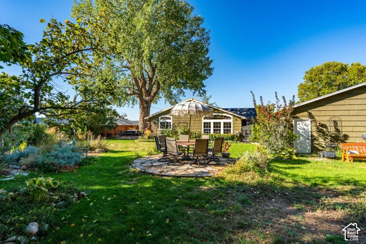 Expansive backyard featuring a natural stone patio, mature trees, landscaped garden beds, and shingle-style exterior siding