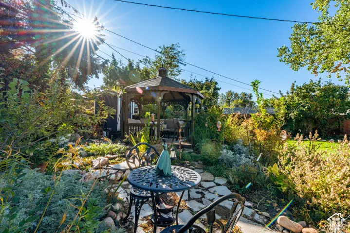 Backyard garden featuring a wood-frame gazebo, flagstone pathway, mature landscaping, and varied perennial shrubs