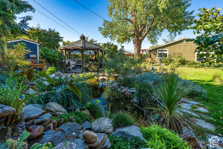 Landscaped backyard featuring a rock-lined pond, hexagonal gazebo, and mature trees