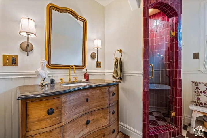 Wood-finish vanity with dark stone countertop, brass faucet, arched shower enclosure with deep-hued glazed tile, and wall-mounted light fixtures