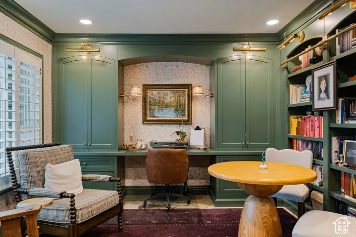 Custom built-in cabinetry with integrated workspace, full-wall shelving, patterned wall covering, brass-finish accent lighting, and shutter-style window treatments