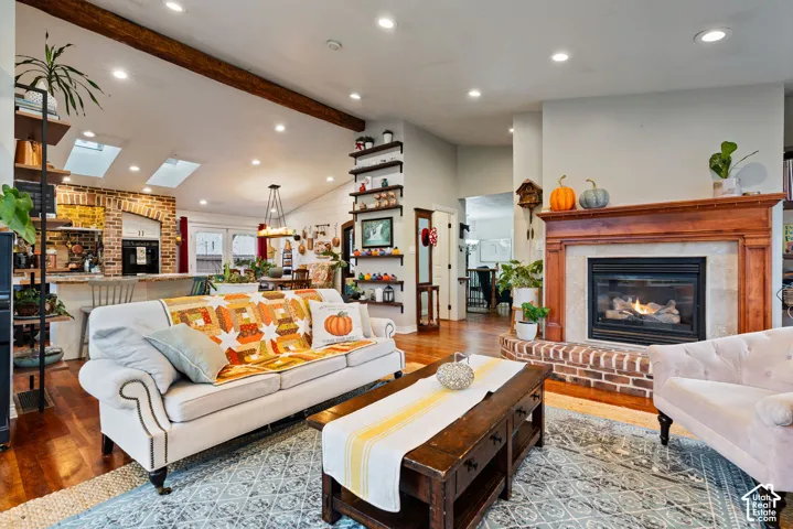 Exposed wood ceiling beams, recessed lighting, brick-surround gas fireplace with a wood mantel, built-in shelving, and skylights