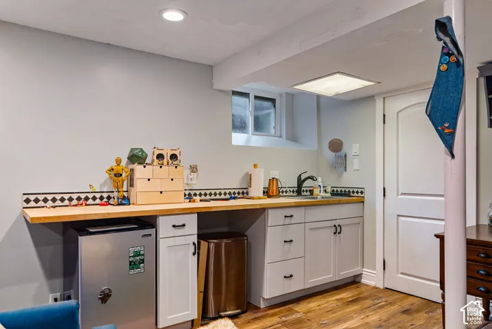 Kitchenette area featuring light-toned cabinetry, wood-surface countertop, decorative tile backsplash, undermount sink with dark-finish hardware, and wood-finish flooring