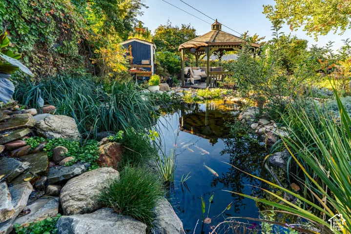 Landscaped koi pond featuring tiered stone edging and lush aquatic plantings, complemented by a detached wooden gazebo and garden storage structure