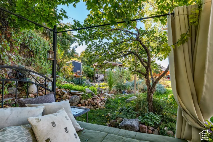 Backyard featuring a tiered stone retaining wall, mature deciduous trees, dense foliage, and a detached wooden structure