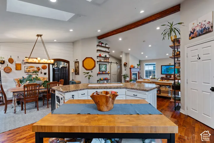 Kitchen featuring a butcher-block topped island, multi-tiered stone-surface peninsula, recessed lighting, wood-finish flooring, and an exposed structural ceiling beam