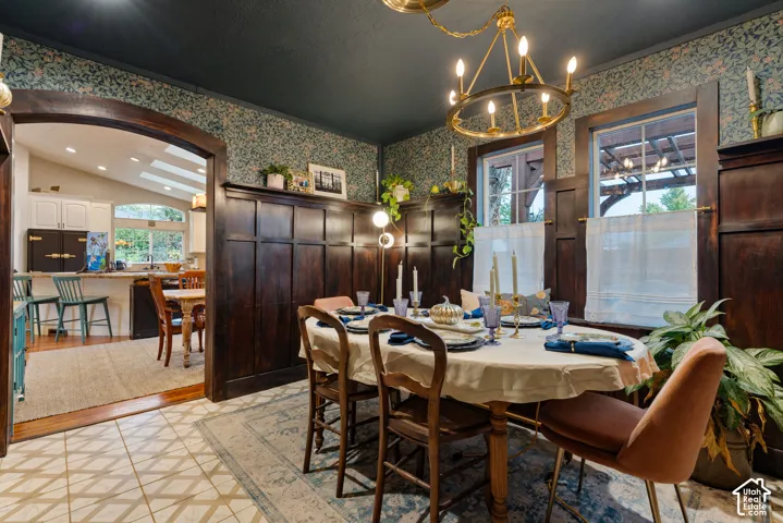 Dining area featuring floor-to-ceiling dark wood wainscoting, patterned wallpaper, a central wagon wheel chandelier, an arched entryway, and tile flooring