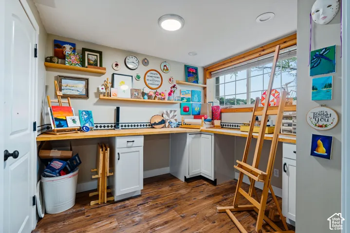 Built-in workspace featuring wood-finish countertops, white cabinetry with matte black hardware, floating wood shelving, and wood-finish flooring
