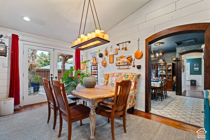 Vaulted ceiling with horizontal plank wall paneling, rectangular multi-light pendant fixture, wood-finish flooring, and a decorative arched wood entryway