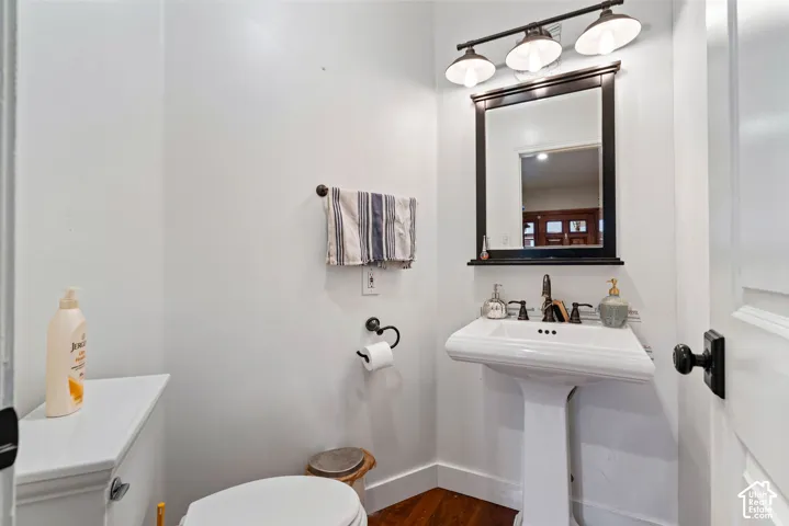 White pedestal sink featuring a widespread faucet, framed wall-mounted mirror, three-light vanity fixture, and wood-finish flooring