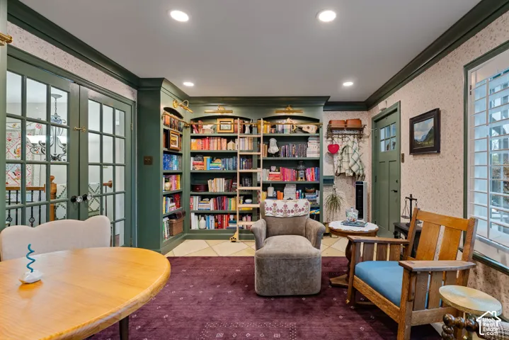 Custom floor-to-ceiling built-in shelving with integrated brass ladder and rail, recessed lighting, multi-pane glass French doors, and plantation shutters
