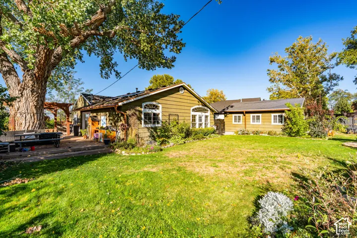 Expansive backyard featuring a mature shade tree, lap siding exterior, arched window detailing, and a timber pergola