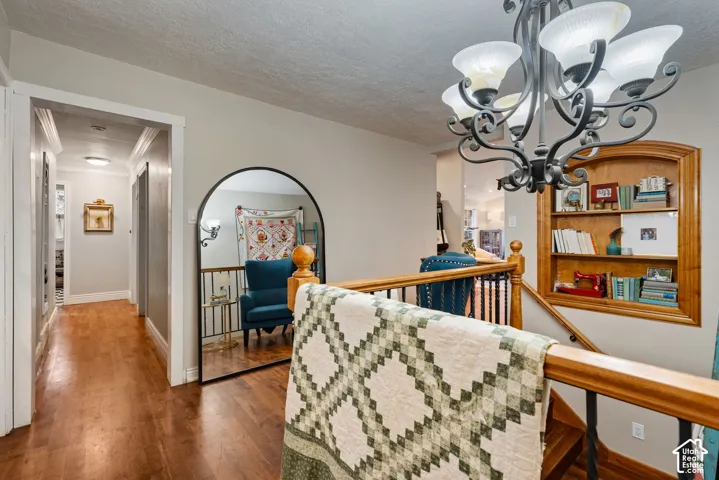 Hardwood flooring, ornate multi-arm chandelier, built-in recessed wall shelving with arched trim, and wood-finish railing with metal balusters