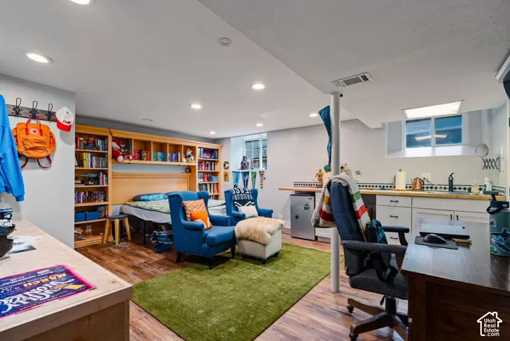 Recessed lighting, wood-finish flooring, built-in wooden shelving, and a kitchenette featuring white cabinetry and a countertop