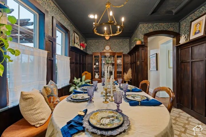 Dining space featuring floor-to-ceiling wood wainscoting, intricate patterned wallpaper, a custom-built wooden hutch, a circular multi-arm chandelier, and arched entryway trim