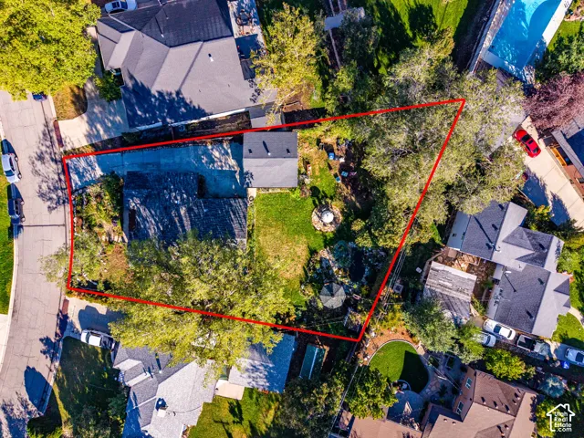 Aerial perspective of a property lot featuring an expansive lawn, mature tree canopy, stone-bordered landscaping, and a concrete driveway