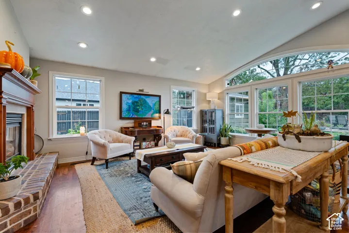 Vaulted ceilings, brick-surround fireplace, wood-finish flooring, and expansive windows featuring multi-pane glass