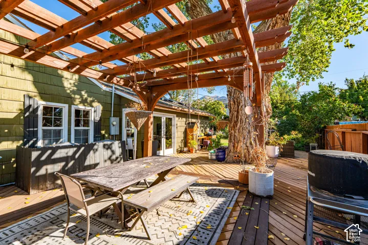 Outdoor wood pergola structure covering a spacious wood deck, featuring cedar-style siding and glass-paneled double doors