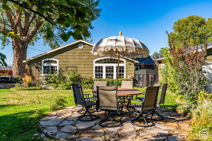 Backyard featuring a stone patio, shake-style siding, arched multi-pane windows, and mature trees