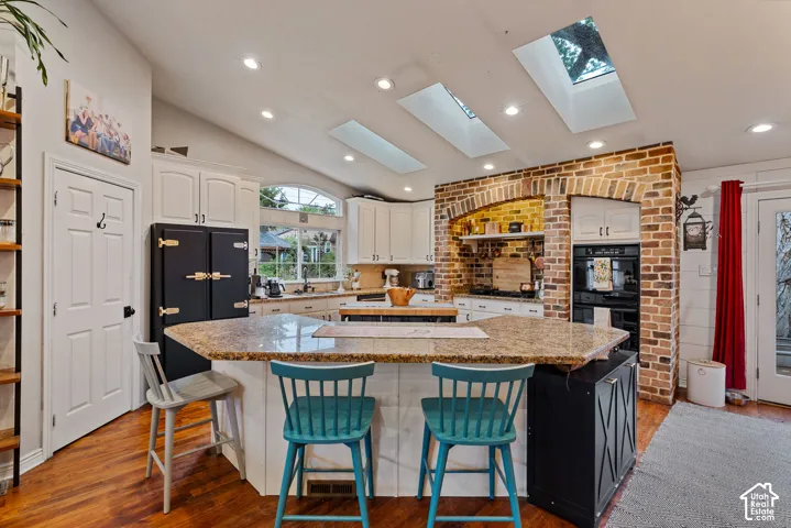 Kitchen featuring a stone-topped peninsula, custom brick archway with built-in oven, three overhead skylights, recessed lighting, and wood-finish flooring