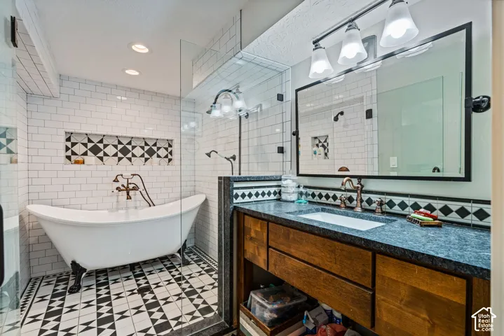 Freestanding clawfoot tub with bridge faucet, glass-enclosed shower, custom wood vanity with stone countertop, and geometric patterned floor tile
