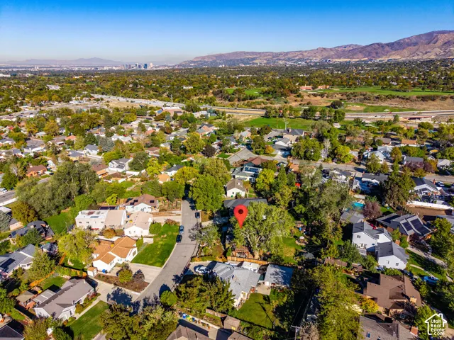 Aerial perspective of a residential property featuring a large tree-lined lot, expansive green space, and a mountainous backdrop