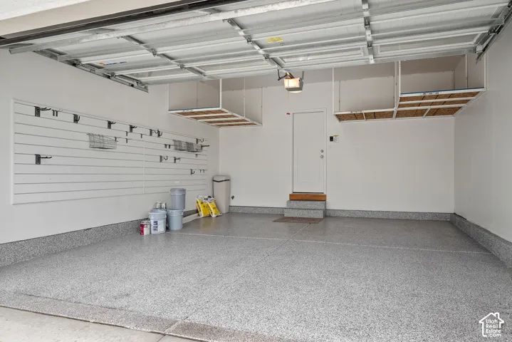 Garage featuring an epoxy floor finish, wall-mounted slat storage system, and dual overhead built-in shelving units