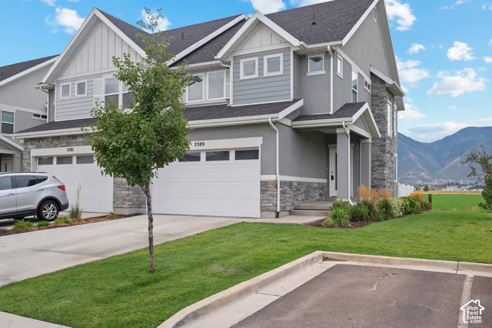 Multi-story exterior featuring a stone and horizontal siding facade, asphalt shingle roof, two-car garage, and mountain backdrop