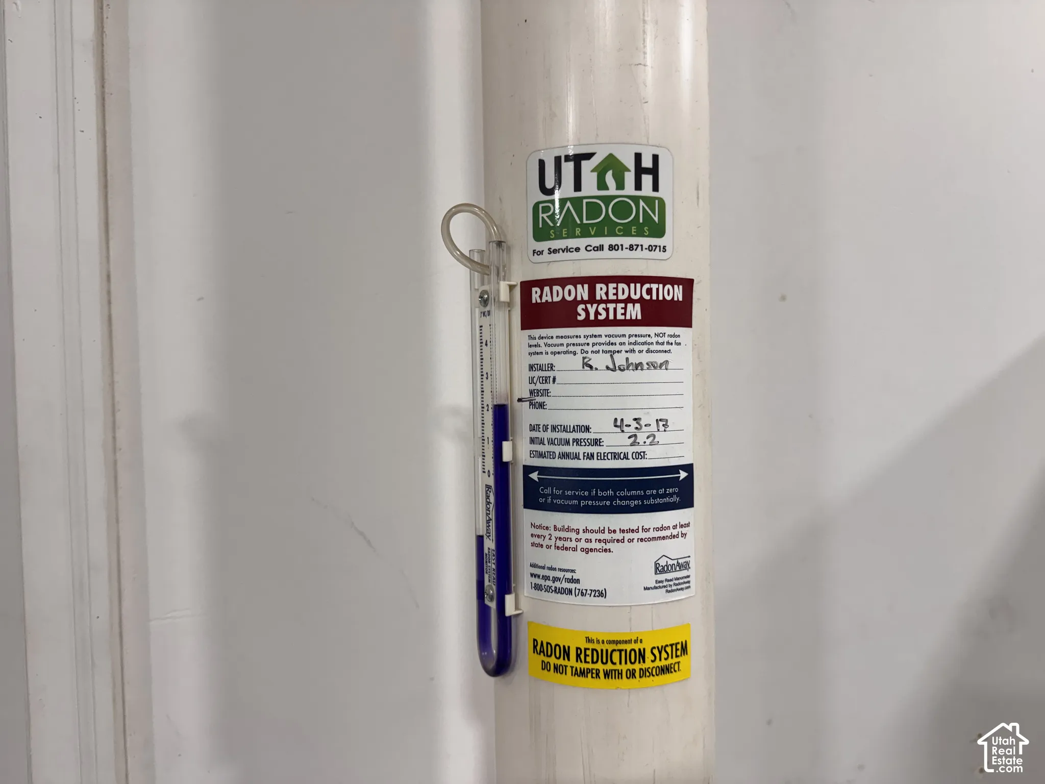 Radon reduction system featuring a vertical pipe, vacuum pressure gauge, and service identification label