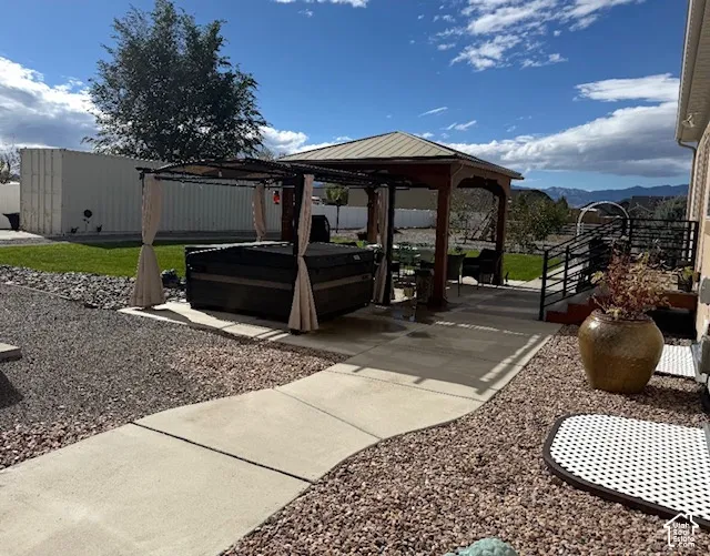 Backyard space featuring a concrete patio, a permanent wood-frame gazebo, a built-in spa, and landscaped gravel beds