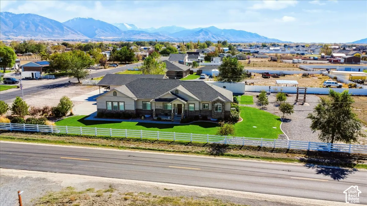 Single-level residence with stone and horizontal siding exterior, asphalt shingle roof, white rail fencing, manicured lawn, and mountain backdrop